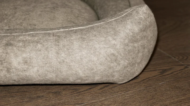 Nahaufnahme einer Bettecke mit Filztextur, Naht und Holzbodenkante